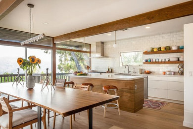 Photo of a contemporary single-wall open plan kitchen in San Francisco with a farmhouse sink, flat-panel cabinets, white cabinets, quartz benchtops, white splashback, ceramic splashback, stainless steel appliances, light hardwood floors and with island.