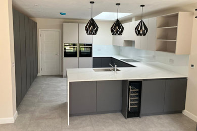 Design ideas for a medium sized urban grey and white u-shaped open plan kitchen in London with a built-in sink, flat-panel cabinets, grey cabinets, white splashback, integrated appliances, a breakfast bar, grey floors and white worktops.