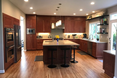 Open concept kitchen - large transitional u-shaped medium tone wood floor and brown floor open concept kitchen idea in Portland with a single-bowl sink, recessed-panel cabinets, medium tone wood cabinets, quartz countertops, gray backsplash, ceramic backsplash, stainless steel appliances, an island and beige countertops