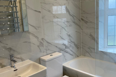 Photo of a medium sized modern ensuite bathroom in London with white cabinets, a built-in bath, a shower/bath combination, a two-piece toilet, black and white tiles, porcelain tiles, porcelain flooring, a wall-mounted sink, a hinged door, a single sink and a floating vanity unit.