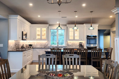 Example of a large transitional l-shaped medium tone wood floor and vaulted ceiling open concept kitchen design in Boston with a farmhouse sink, beaded inset cabinets, white cabinets, granite countertops, gray backsplash, mosaic tile backsplash, stainless steel appliances, an island and black countertops