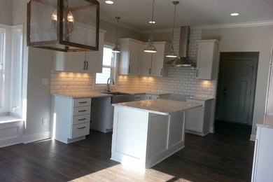 This is an example of a country kitchen in Grand Rapids with a farmhouse sink, shaker cabinets, white cabinets, quartzite benchtops, white splashback, ceramic splashback, stainless steel appliances and with island.