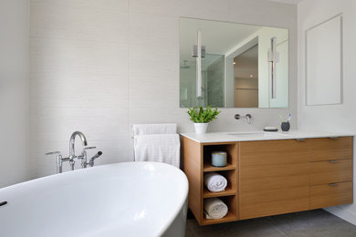 Design ideas for a mid-sized modern master bathroom in Toronto with flat-panel cabinets, light wood cabinets, a freestanding tub, a corner shower, a one-piece toilet, white tile, ceramic tile, white walls, porcelain floors, an undermount sink, solid surface benchtops and grey floor.