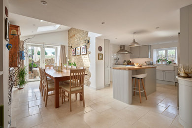Photo of a small traditional kitchen/dining room in Oxfordshire with white walls, porcelain flooring, a wood burning stove, a stone fireplace surround, beige floors, brick walls and a feature wall.