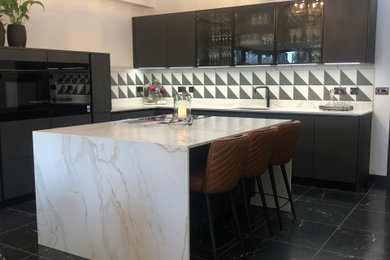 Photo of a large contemporary cream and black l-shaped kitchen/diner in Other with a submerged sink, flat-panel cabinets, black cabinets, granite worktops, multi-coloured splashback, porcelain splashback, porcelain flooring, an island, black floors, white worktops, a vaulted ceiling, feature lighting and integrated appliances.