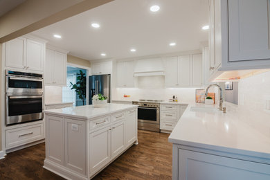 Inspiration for a transitional medium tone wood floor and brown floor kitchen remodel in DC Metro with an undermount sink, recessed-panel cabinets, white cabinets, quartz countertops, white backsplash, ceramic backsplash, stainless steel appliances, an island and white countertops