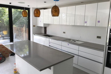 Diseño de cocina comedor lineal moderna de tamaño medio con armarios con paneles lisos, puertas de armario blancas, encimera de cuarcita, electrodomésticos de acero inoxidable y una isla