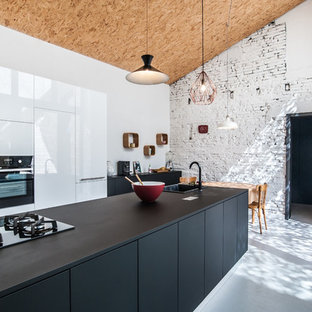 Cette image montre une cuisine américaine design avec un évier 1 bac, un placard à porte plane, des portes de placard blanches, un électroménager noir et un îlot central.