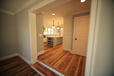 Example of a galley medium tone wood floor enclosed kitchen design in Baltimore with white cabinets, stainless steel appliances, an island, ceramic backsplash, a farmhouse sink, white backsplash and quartz countertops