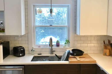 Mid-sized l-shaped open plan kitchen in Portland Maine with an undermount sink, flat-panel cabinets, white cabinets, granite benchtops, white splashback, porcelain splashback, stainless steel appliances, porcelain floors, with island and beige floor.
