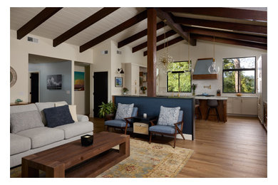 Large transitional open concept medium tone wood floor, multicolored floor, exposed beam and wallpaper living room photo in Other with white walls, a standard fireplace, a stone fireplace and a wall-mounted tv