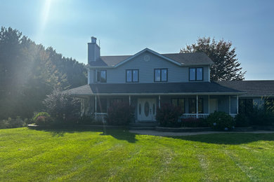 Modelo de fachada de casa azul y gris de estilo de casa de campo grande de dos plantas con revestimiento de vinilo, techo de mariposa, tejado de teja de madera y tablilla