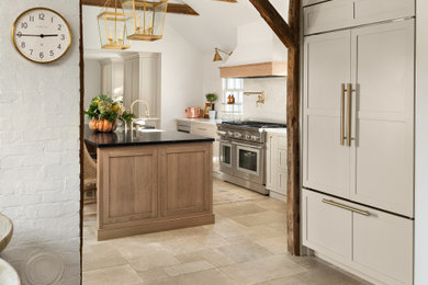 Inspiration for a large transitional porcelain tile, beige floor and exposed beam kitchen remodel in New York with a farmhouse sink, shaker cabinets, beige cabinets, soapstone countertops, beige backsplash, stainless steel appliances, an island and black countertops