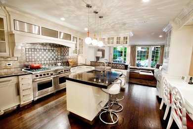 Example of a large transitional u-shaped dark wood floor and brown floor enclosed kitchen design in Los Angeles with a farmhouse sink, granite countertops, stainless steel appliances, an island and black countertops