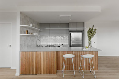This is an example of a mid-sized modern u-shaped open plan kitchen in Sydney with an undermount sink, flat-panel cabinets, grey cabinets, quartz benchtops, white splashback, ceramic splashback, stainless steel appliances, laminate floors, with island, brown floor and white benchtop.