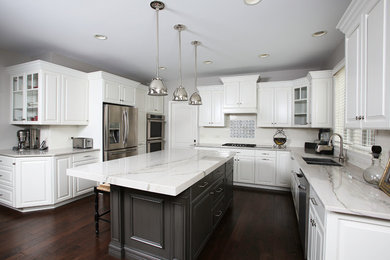 Large transitional u-shaped dark wood floor and brown floor eat-in kitchen photo in Chicago with white cabinets, white backsplash, stainless steel appliances, an island, a double-bowl sink, raised-panel cabinets, marble countertops and subway tile backsplash