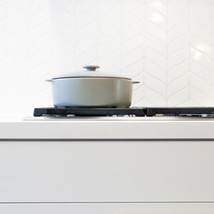 Cette photo montre une grande arrière-cuisine éclectique en U avec un évier encastré, un placard à porte shaker, des portes de placard blanches, un plan de travail en quartz modifié, une crédence jaune, une crédence en carreau de céramique, un électroménager noir, un sol en bois brun, un îlot central et un sol marron.