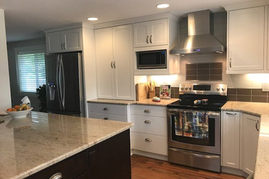Mid-sized transitional l-shaped eat-in kitchen in Portland with an undermount sink, recessed-panel cabinets, white cabinets, granite benchtops, multi-coloured splashback, porcelain splashback, stainless steel appliances, medium hardwood floors, with island, brown floor and multi-coloured benchtop.