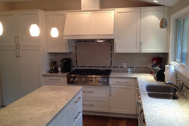 Large trendy l-shaped medium tone wood floor and brown floor eat-in kitchen photo in New York with an undermount sink, recessed-panel cabinets, white cabinets, granite countertops, white backsplash, ceramic backsplash, stainless steel appliances, an island and gray countertops