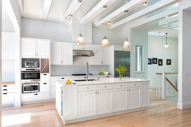 Example of a mid-sized transitional l-shaped light wood floor kitchen pantry design in San Francisco with a drop-in sink, recessed-panel cabinets, white cabinets, stainless steel appliances and an island