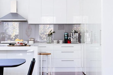 Photo of a large contemporary l-shaped eat-in kitchen in Melbourne with flat-panel cabinets, white cabinets, quartz benchtops, white splashback, stainless steel appliances, dark hardwood floors, with island, glass tile splashback and brown floor.