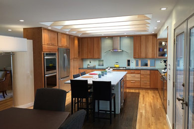 This is an example of a mid-sized contemporary u-shaped eat-in kitchen in DC Metro with an undermount sink, flat-panel cabinets, medium wood cabinets, solid surface benchtops, grey splashback, stainless steel appliances, light hardwood floors, with island, beige floor and black benchtop.