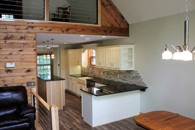 Example of a mid-sized trendy u-shaped vinyl floor and brown floor eat-in kitchen design in Other with a farmhouse sink, raised-panel cabinets, white cabinets, granite countertops, gray backsplash, stone tile backsplash, stainless steel appliances, an island and black countertops