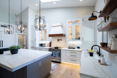 Inspiration for a mid-sized cottage l-shaped light wood floor, brown floor and vaulted ceiling eat-in kitchen remodel in Phoenix with an undermount sink, recessed-panel cabinets, white cabinets, quartz countertops, white backsplash, porcelain backsplash, paneled appliances, an island and white countertops