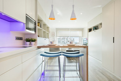 Photo of a mid-sized modern single-wall open plan kitchen in Barcelona with a drop-in sink, flat-panel cabinets, white cabinets, quartz benchtops, white splashback, panelled appliances, porcelain floors and a peninsula.