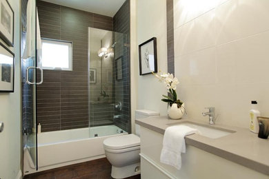 Mid-sized contemporary 3/4 bathroom in Los Angeles with flat-panel cabinets, white cabinets, an alcove tub, a shower/bathtub combo, a two-piece toilet, brown tile, gray tile, white tile, porcelain tile, white walls, dark hardwood floors, an undermount sink, engineered quartz benchtops, brown floor and a hinged shower door.
