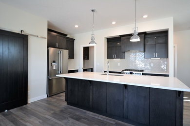 Inspiration for a mid-sized transitional single-wall brown floor and laminate floor open concept kitchen remodel in Calgary with an undermount sink, flat-panel cabinets, dark wood cabinets, quartz countertops, porcelain backsplash, stainless steel appliances, an island and gray backsplash
