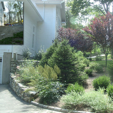 Stone retaining walls and plantings hide house foundation. Evergreen and floweri