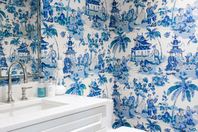 Powder room - small transitional light wood floor and wallpaper powder room idea in Miami with raised-panel cabinets, white cabinets, a one-piece toilet, marble countertops, white countertops and a built-in vanity