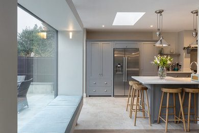 Photo of a large transitional galley eat-in kitchen in Hertfordshire with a farmhouse sink, shaker cabinets, grey cabinets, marble benchtops, white splashback, marble splashback, stainless steel appliances, ceramic floors, with island, beige floor and white benchtop.