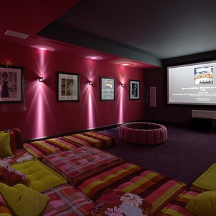 Cette image montre une grande salle de cinéma design fermée avec un mur rose, moquette, un écran de projection et un sol violet.