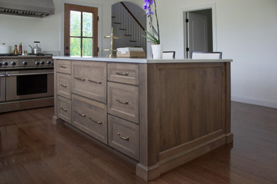 Example of a large transitional u-shaped medium tone wood floor and brown floor kitchen design in New York with a farmhouse sink, recessed-panel cabinets, medium tone wood cabinets, quartz countertops, stainless steel appliances, an island and white countertops