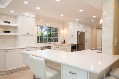 Mid-sized transitional l-shaped porcelain tile and beige floor eat-in kitchen photo in Los Angeles with an undermount sink, recessed-panel cabinets, white cabinets, quartz countertops, white backsplash, glass tile backsplash, stainless steel appliances, a peninsula and white countertops
