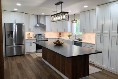 Inspiration for a mid-sized country l-shaped vinyl floor and brown floor eat-in kitchen remodel in Atlanta with a farmhouse sink, shaker cabinets, white cabinets, granite countertops, white backsplash, subway tile backsplash, stainless steel appliances, an island and black countertops