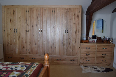 Photo of a large traditional built-in wardrobe in Buckinghamshire with beaded cabinets, medium wood cabinets, carpet, beige floors and exposed beams.
