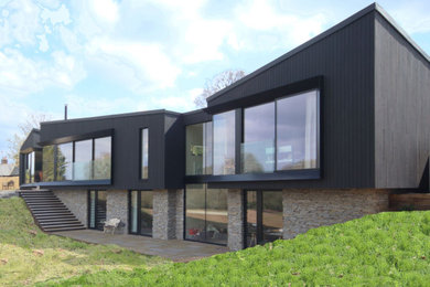 This is an example of a medium sized and black contemporary two floor rear detached house in Surrey with wood cladding, a flat roof, a green roof and board and batten cladding.