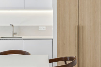 Inspiration pour une cuisine américaine linéaire, encastrable, bicolore et blanche et bois design en bois clair de taille moyenne avec un évier 1 bac, un placard à porte plane, un plan de travail en quartz, une crédence beige, une crédence en quartz modifié, parquet clair, îlot et un plan de travail beige.