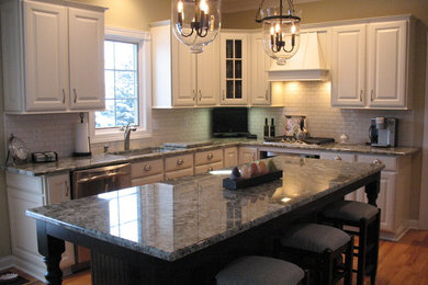 Mid-sized elegant l-shaped light wood floor open concept kitchen photo in New York with an undermount sink, raised-panel cabinets, white cabinets, granite countertops, white backsplash, subway tile backsplash, stainless steel appliances and an island