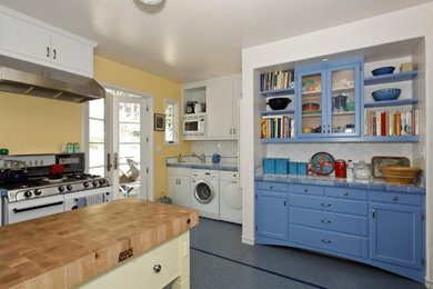 Example of a mid-sized classic l-shaped terrazzo floor and blue floor kitchen pantry design in San Francisco with shaker cabinets, blue cabinets, tile countertops, white backsplash, ceramic backsplash, white appliances and an island