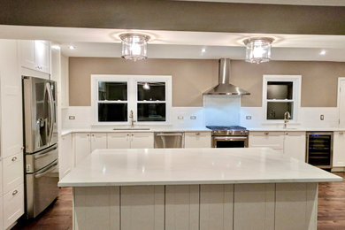 Example of a large transitional l-shaped medium tone wood floor eat-in kitchen design in Seattle with an undermount sink, white cabinets, quartz countertops, white backsplash, ceramic backsplash, stainless steel appliances, an island and white countertops