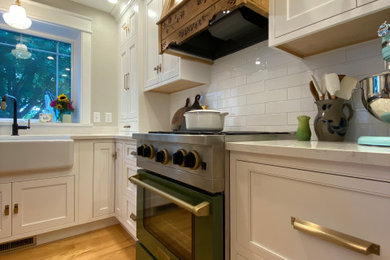 This is an example of a medium sized traditional l-shaped open plan kitchen in Milwaukee with a belfast sink, beaded cabinets, white cabinets, engineered stone countertops, white splashback, porcelain splashback, white appliances, medium hardwood flooring, an island, brown floors and white worktops.