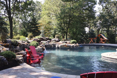 Large traditional backyard custom-shaped natural pool in New York with a water feature and concrete pavers.