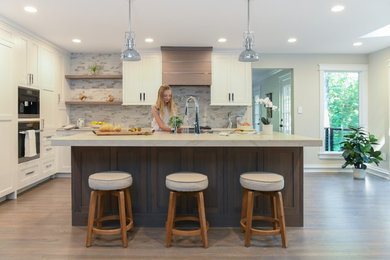 Example of a mid-sized trendy l-shaped medium tone wood floor and brown floor kitchen pantry design in DC Metro with a farmhouse sink, shaker cabinets, medium tone wood cabinets, quartzite countertops, multicolored backsplash, porcelain backsplash, paneled appliances, an island and white countertops