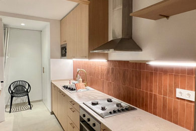 Diseño de cocina alargada y blanca y madera mediterránea de tamaño medio cerrada sin isla con fregadero encastrado, armarios con paneles lisos, puertas de armario de madera clara, encimera de cuarzo compacto, salpicadero rojo, salpicadero de azulejos de cerámica, electrodomésticos de acero inoxidable, suelo de baldosas de cerámica, suelo gris, encimeras beige y barras de cocina