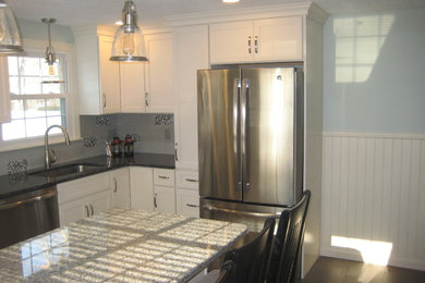 Mid-sized elegant u-shaped medium tone wood floor and brown floor enclosed kitchen photo in Boston with an undermount sink, shaker cabinets, white cabinets, granite countertops, gray backsplash, subway tile backsplash, stainless steel appliances and an island