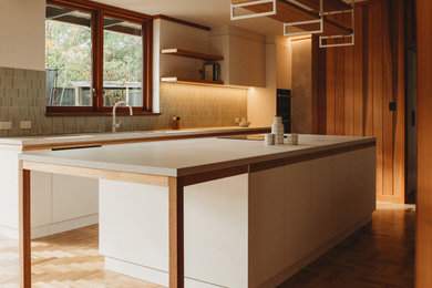 Design ideas for a large midcentury u-shaped kitchen pantry in Adelaide with a double-bowl sink, flat-panel cabinets, white cabinets, quartz benchtops, green splashback, porcelain splashback, white appliances, medium hardwood floors, with island, brown floor, white benchtop and exposed beam.